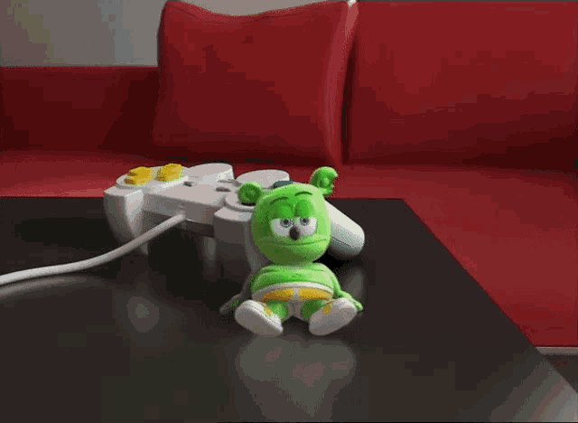 a green gummy bear sits on a table next to a game controller