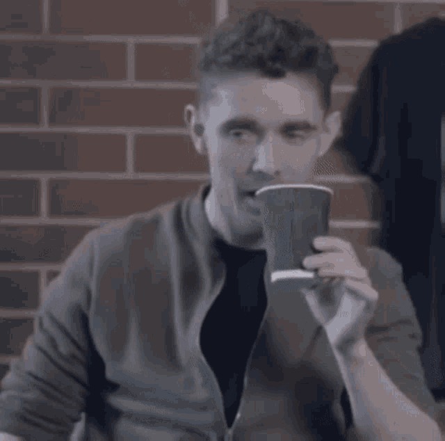 a man in a green jacket is drinking from a cup