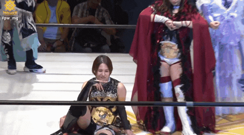 a woman in a red cape is sitting on the floor in a wrestling ring