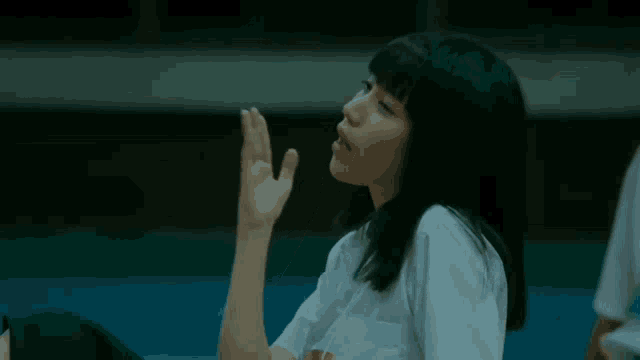 a young girl in a white shirt is sitting on the floor with her hand up .