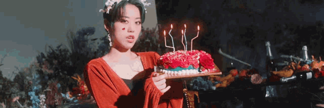 a woman in a red dress is holding a birthday cake with candles .