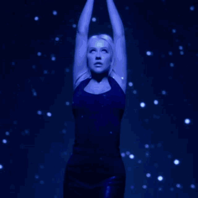 a woman in a black tank top is standing with her arms up in the air