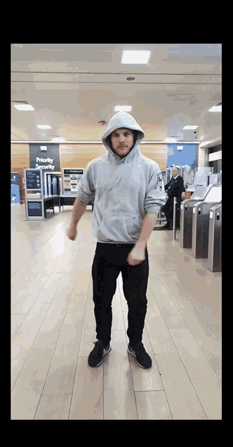 a man in a grey hoodie stands in front of a sign that says " priority check "
