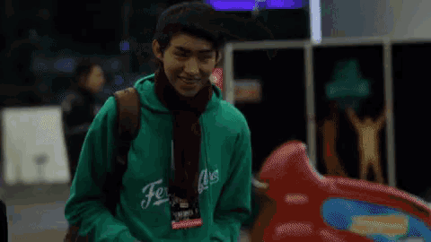 a young man wearing a green hoodie and a scarf smiles