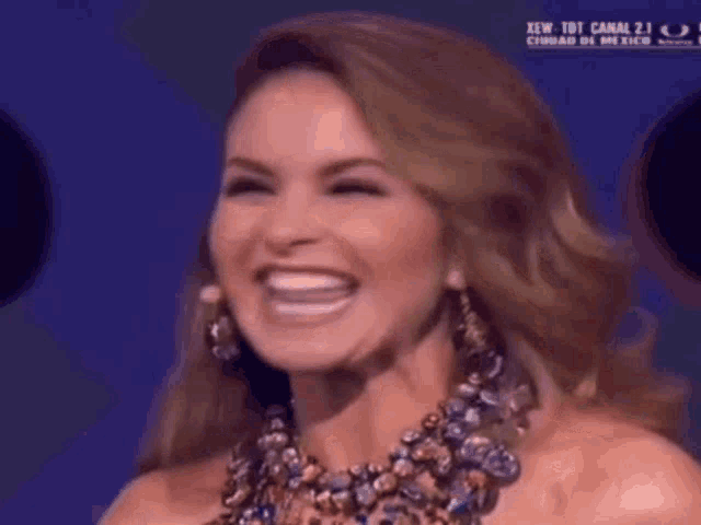 a woman wearing a necklace and earrings is smiling and laughing .