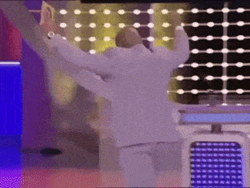 a man in a white suit is dancing in front of a colorful backdrop