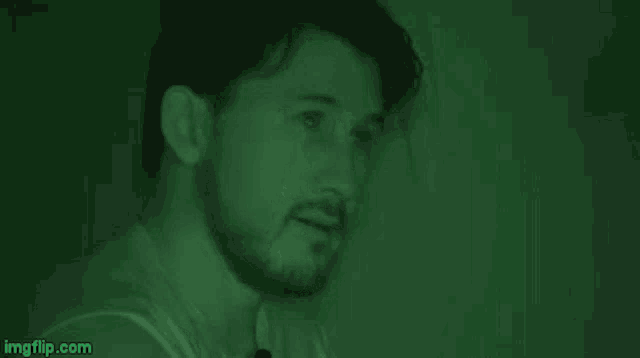 a man with a beard is smiling and looking at the camera in a dark room .