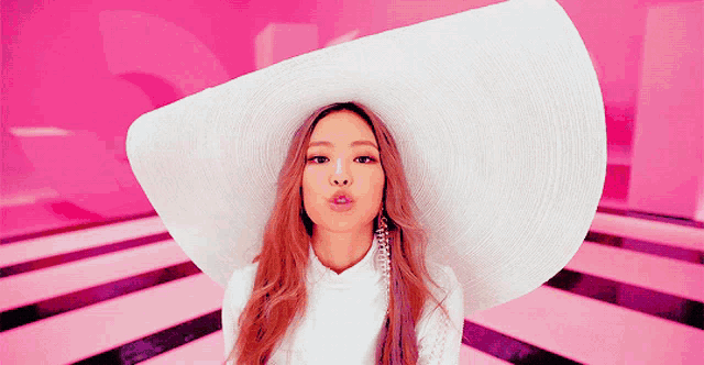 a woman wearing a white hat and earrings blowing a kiss