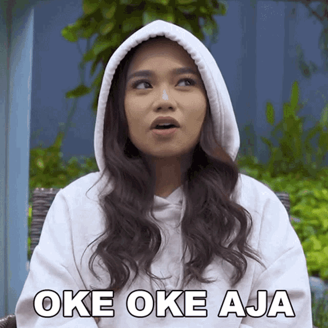 a woman wearing a white hoodie with the words oke oke aja written on it