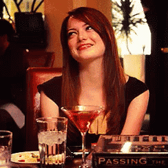 a woman is sitting at a table with a martini glass and a book called passing the time