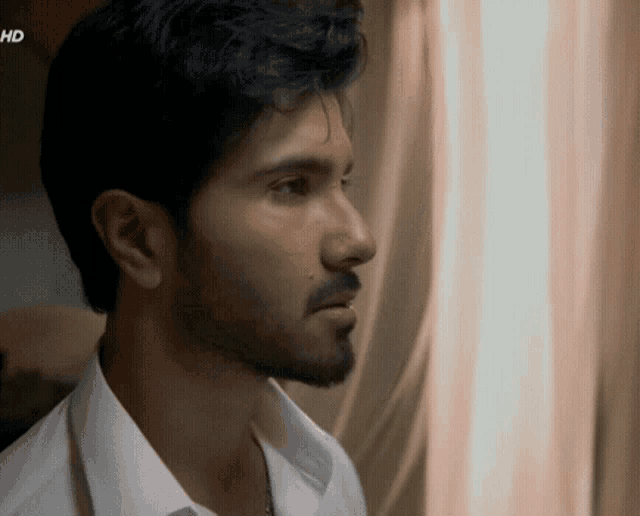 a man with a beard and a white shirt is looking out a window