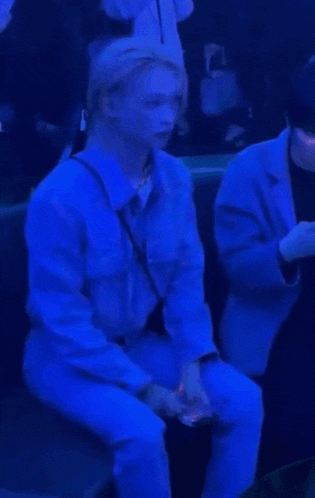 a man in a blue shirt and blue pants is sitting in a crowd of people .