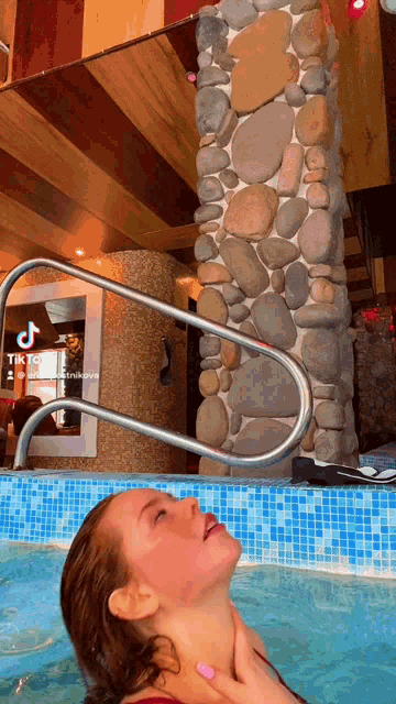 a woman is in a pool with a stone wall behind her