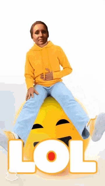 a man in a yellow hoodie is sitting on a large yellow smiley face with the word lol written on it