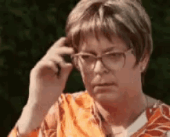 a woman wearing glasses and an orange shirt is scratching her forehead .