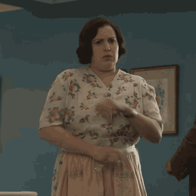 a woman wearing a floral shirt and apron stands with her arms crossed