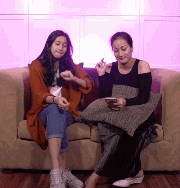 two women are sitting on a couch and one is looking at her phone