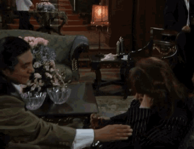 a man and woman are sitting in a living room with flowers on the table