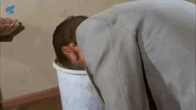 a man is kneeling down in front of a trash can and drinking from it .
