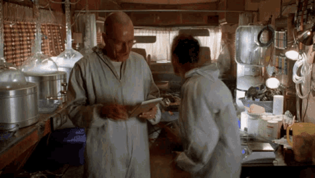 a man in a lab coat looks at a tablet while a woman looks on