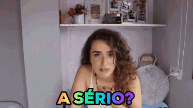 a woman with curly hair says a serio while sitting on a bed