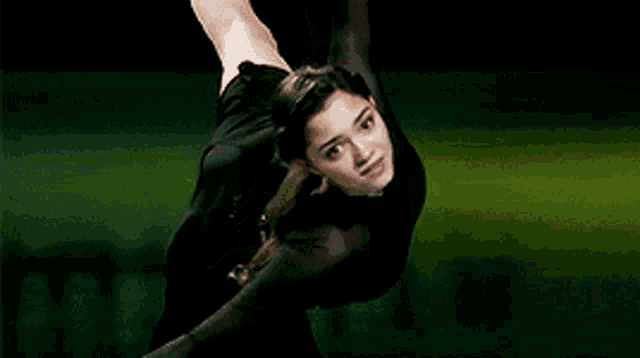 a woman in a black dress is doing a trick on a green background .