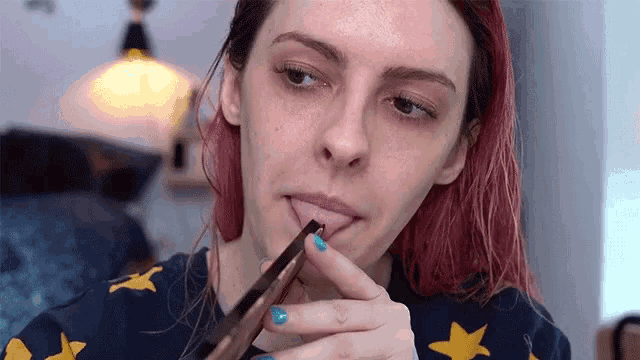 a woman with red hair and blue nails is applying makeup