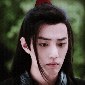 a young man with long black hair has a red ponytail on top of his head