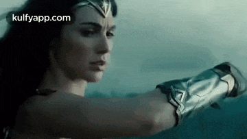 wonder woman is holding a sword in her hand in a movie .