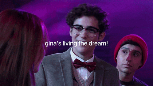 a group of people are standing in front of a stage with purple lights behind them and one of them is wearing glasses