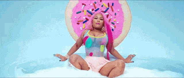 a woman with pink hair is sitting in a bathtub with a pink donut on her head .