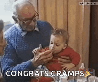 an older man is feeding a baby with a spoon and the baby is eating .