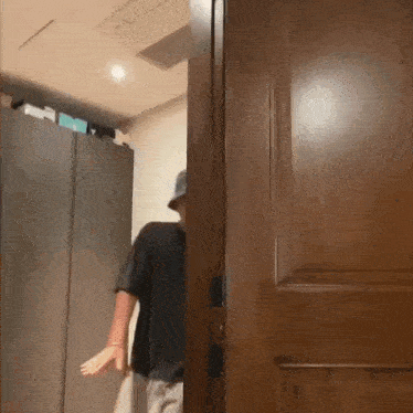 a man in a hat is standing in a room with a wooden door open .