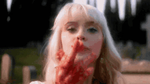a woman with blood on her face is holding a bloody hand .