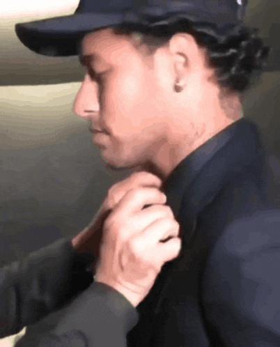 a man wearing a hat and a black jacket is adjusting his tie
