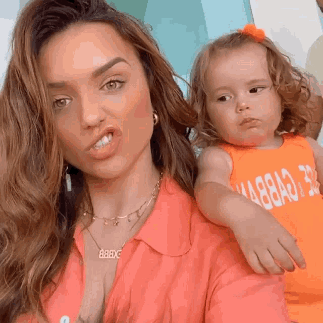 a woman is holding a little girl who is wearing an orange shirt that says ' ma88ad ' on it