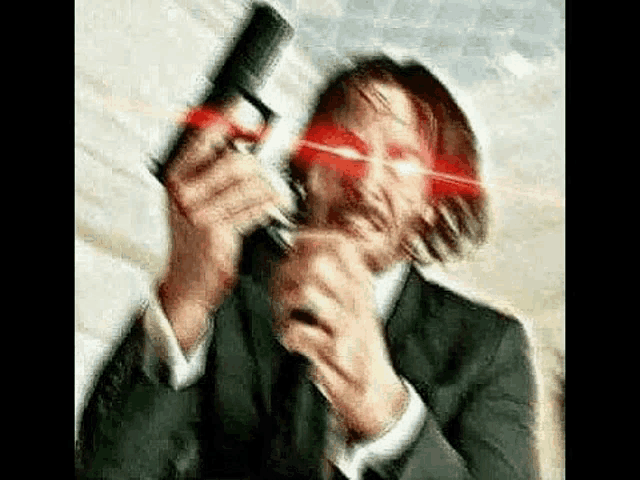 a man in a suit and tie is holding a gun in front of his face with a red light coming out of his eyes .