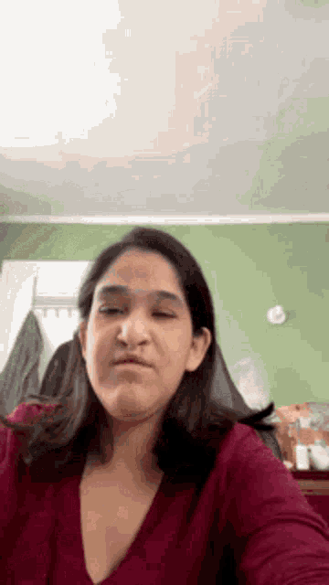 a woman in a red shirt is making a funny face in a bedroom .