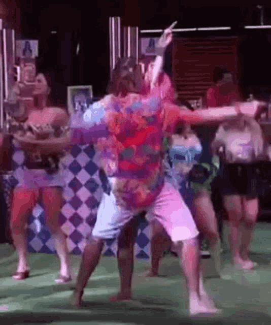 a man in a colorful shirt is dancing with a group of women .