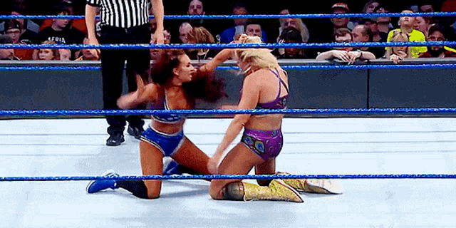 two women are wrestling in a wrestling ring with a referee in the background .
