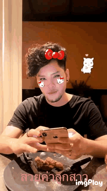 a man is sitting at a table looking at his phone with a hello kitty face filter