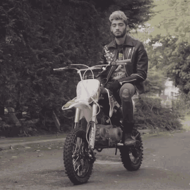 a man in a leather jacket is riding a dirt bike with a sticker on the front that says ' nirvana '