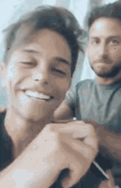 two men are sitting next to each other and smiling . one of the men is wearing a ring on his finger .