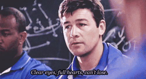 a man in a blue shirt is standing in front of a blackboard with the words clear eyes full hearts can 't lose .