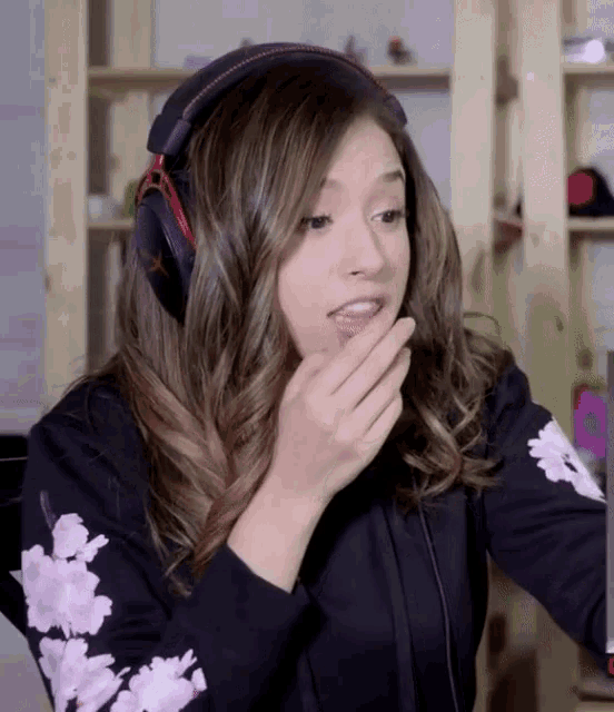 a woman wearing headphones and a black shirt with flowers on the sleeves looks surprised