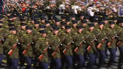 a large group of soldiers marching in a line with a band in the background