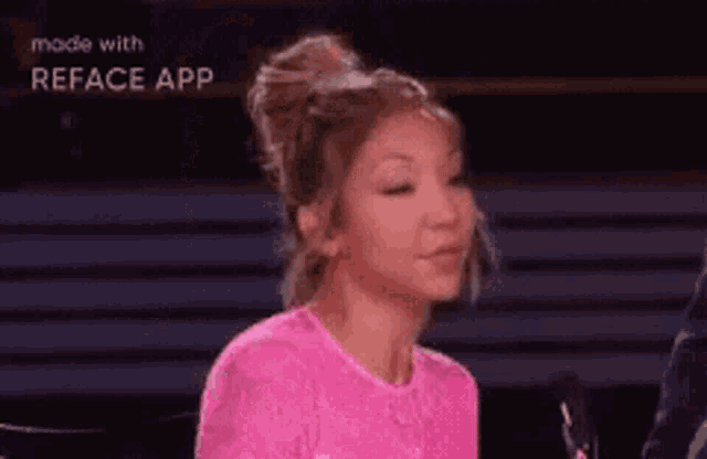 a woman in a pink shirt is talking into a microphone on a stage .