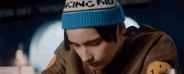 a man wearing a blue beanie and a green jacket is sitting at a table .