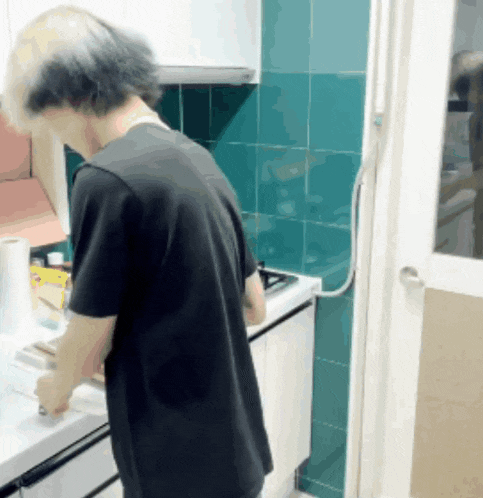 a man in a black shirt stands in a kitchen