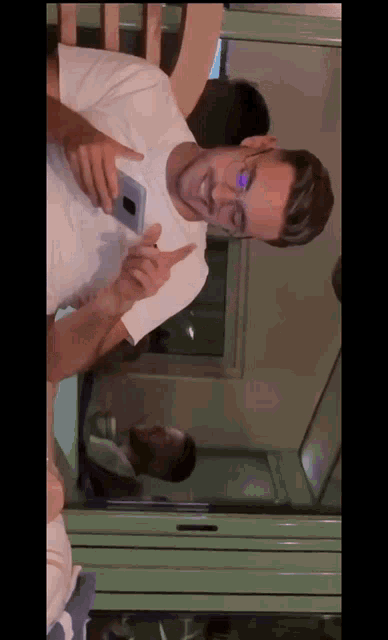 a man in a white shirt is holding a cell phone and pointing